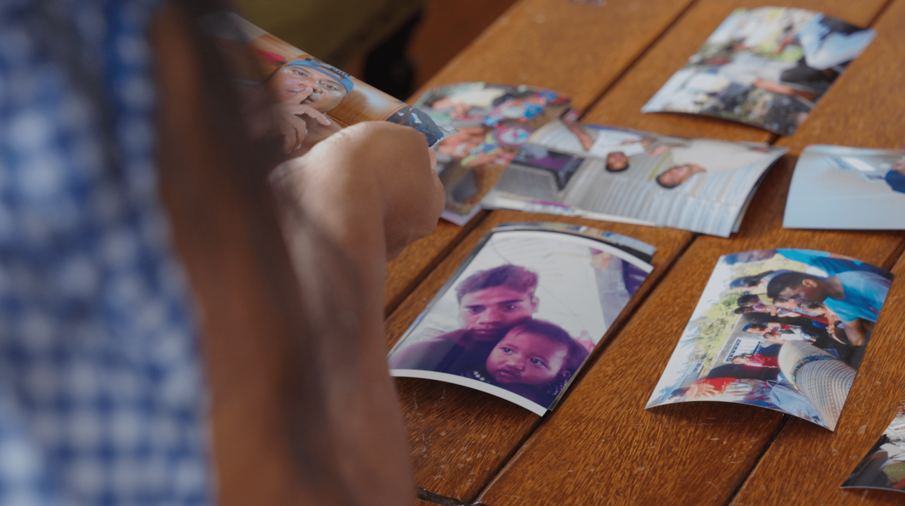 Eritara's family member looking through photographs placed on a wooden table with a focus on a photo of Eritara and his child